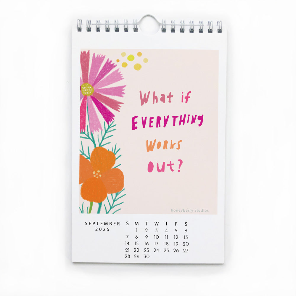 2025 wall calendar page for September featuring colorful floral illustration and inspirational quote "What if everything works out?" on beige background with spiral binding and metal hanger