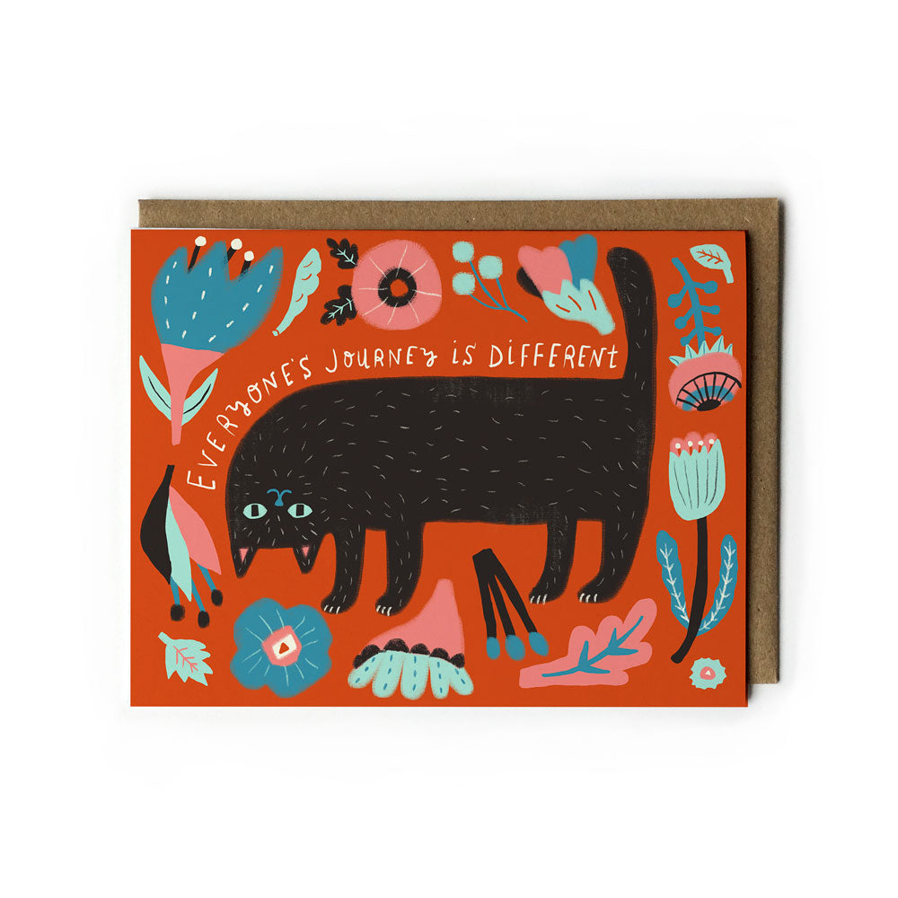 Colorful greeting card featuring a stylized black cat surrounded by floral designs on an orange background, with text reading "Everyone's journey is different" and a matching kraft paper envelope