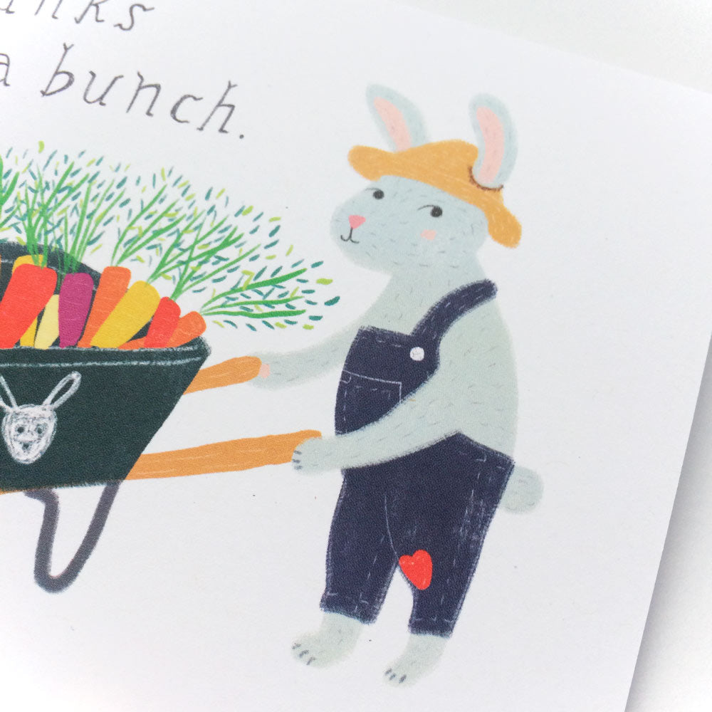 Cute cartoon bunny in overalls pushing wheelbarrow filled with colorful carrots and greens, part of a thank you card design