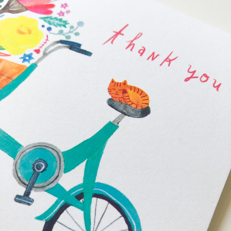 Colorful thank you card featuring a teal bicycle with an orange cat on the seat, surrounded by vibrant flowers and handwritten text