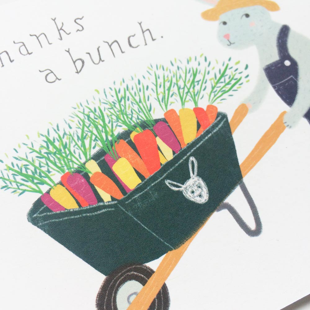 Cute thank you card illustration featuring a blue rabbit pushing a wheelbarrow filled with colorful carrots, with text "thanks a bunch" above, perfect for gardeners or bunny lovers