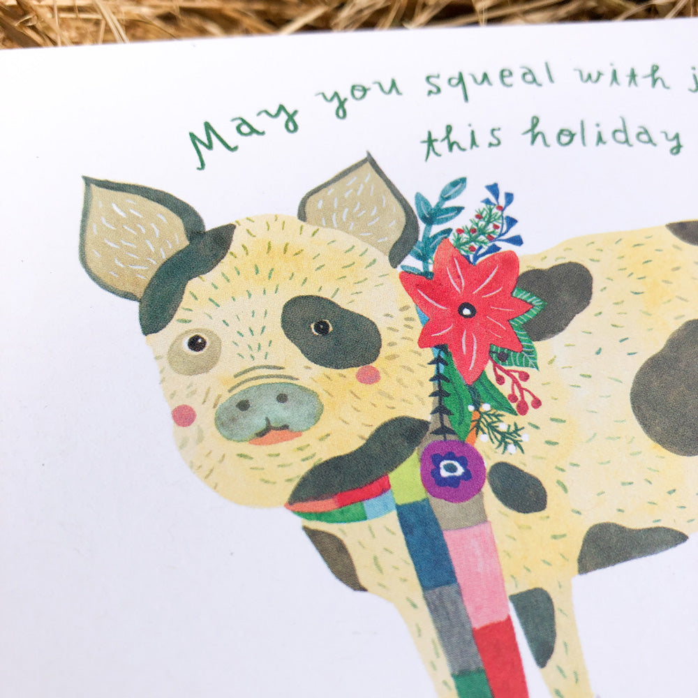 Watercolor greeting card featuring a cheerful spotted pig with a colorful scarf and festive flower, text reads "May you squeal with joy this holiday