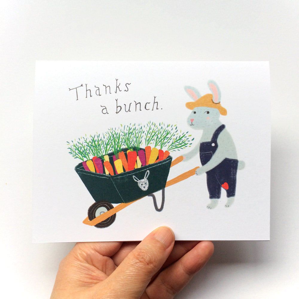 Cute thank you card featuring a cartoon bunny in overalls pushing a wheelbarrow full of colorful carrots, with text "Thanks a bunch" in handwritten style