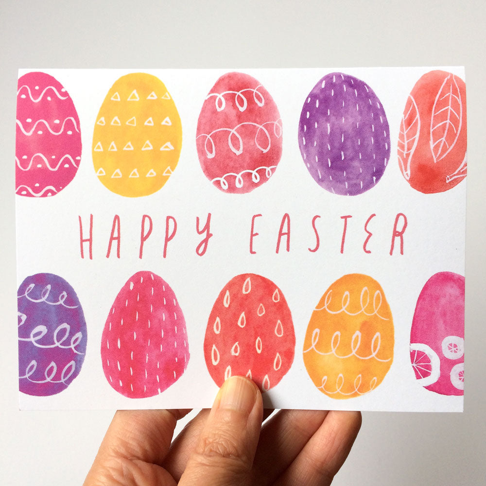 Colorful watercolor Easter egg greeting card with decorative patterns, featuring pink, yellow, purple, and orange eggs surrounding "Happy Easter" text, held by a hand against a white background