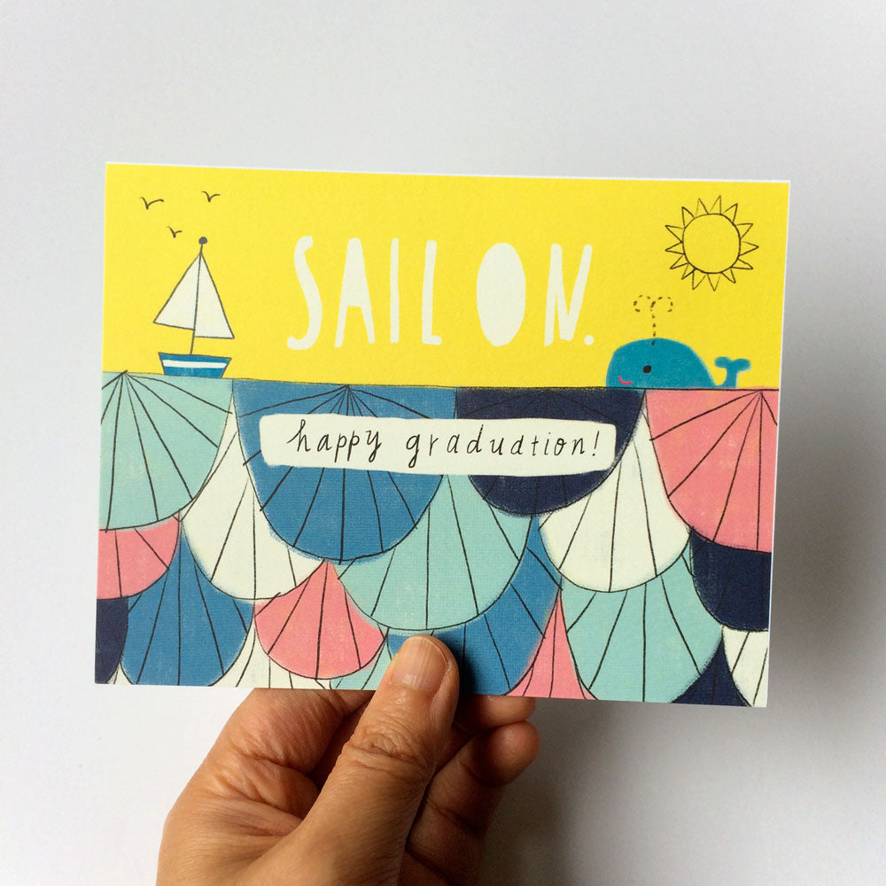 Colorful graduation card featuring a sailboat, whale, and ocean waves with "Sail On" and "happy graduation!" text, held by a hand against a white background, perfect for congratulating graduates