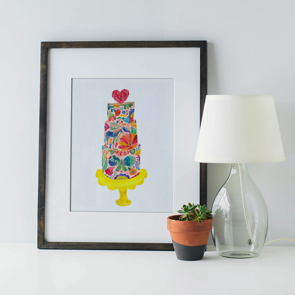 Original watercolor painting of a colorful floral wedding cake on yellow stand, framed and displayed with lamp and potted plant, perfect for wedding decor or gift